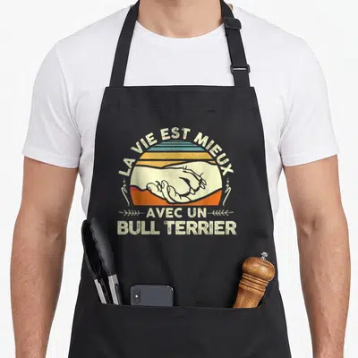 Tablier de cuisine noir avec illustration vintage de deux mains se tenant devant un soleil orange et texte « La vie est mieux avec un Bull Terrier ».