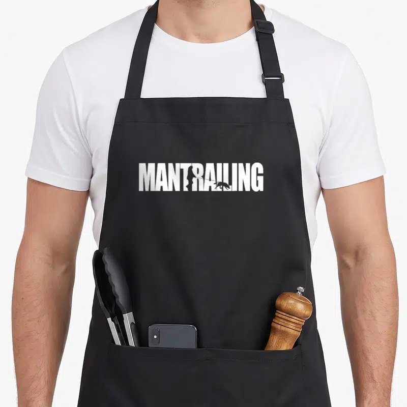 Tablier de cuisine noir avec le texte blanc MANTRAILING et une silhouette de chien suivant une ligne de traçage.