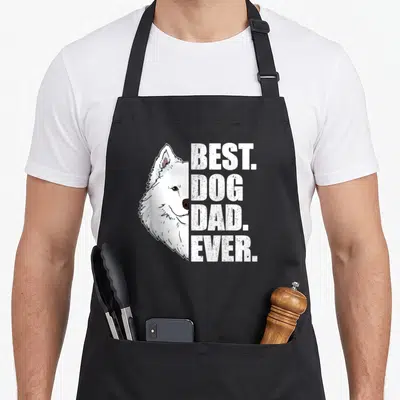 Tablier de cuisine noir avec illustration d'un Samoyed blanc et le texte BEST. DOG. DAD. EVER. en lettres capitales blanches.