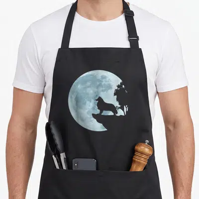 Tablier de cuisine noir avec silhouette de chien face à une pleine lune bleue stylisée et un arbre en arrière-plan.