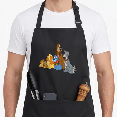Tablier de cuisine noir avec Lady, Tramp et leurs petits chiots dessinés en couleur au centre du vêtement.