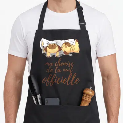 Tablier de cuisine noir avec deux chiens dorment sous une couverture et le texte « ma chemise de la nuit » en lettres cursive.