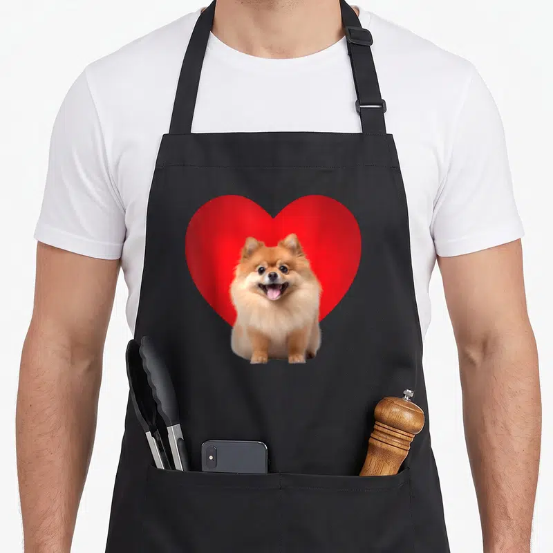 Tablier de cuisine noir avec un Pomeranian devant un grand Coeur rouge vif.