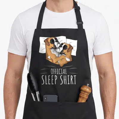 Tablier de cuisine noir avec deux chiens Boxers blottis dans un lit et le texte OFFICIAL SLEEP SHIRT imprimé en blanc.