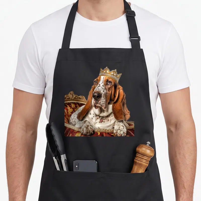 Tablier de cuisine noir avec illustration d'un Basset Hound couronné assis sur un fauteuil royal rouge et doré.