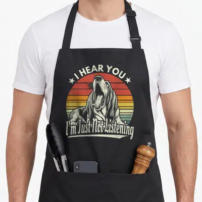 Tablier de cuisine noir avec un basset hound qui bâille devant un soleil rayé et le texte « I HEAR YOU I'm Just Not Listening ».