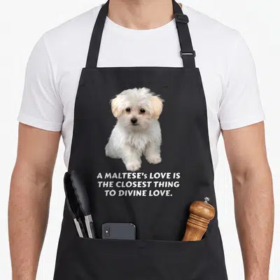 Tablier de cuisine noir avec un chiot maltais blanc et le texte A Maltese's love is the closest thing to divine love imprimé en bas.
