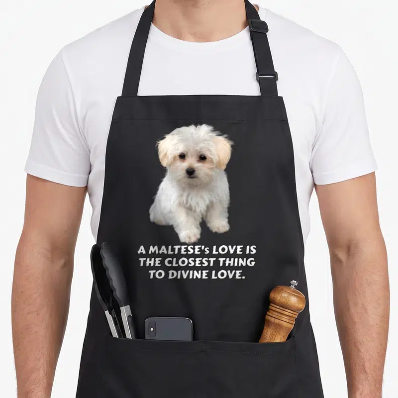 Tablier de cuisine noir avec un chiot maltais blanc et le texte A Maltese's love is the closest thing to divine love imprimé en bas.