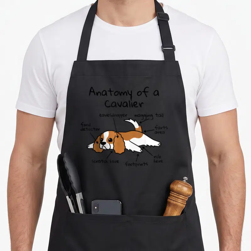 Tablier de cuisine noir avec illustration d'un Cavalier King Charles Spaniel annoté en anglais.