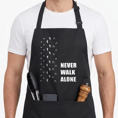 Tablier de cuisine noir avec traces blanches de pattes, pieds et fers à cheval et texte Never Walk Alone