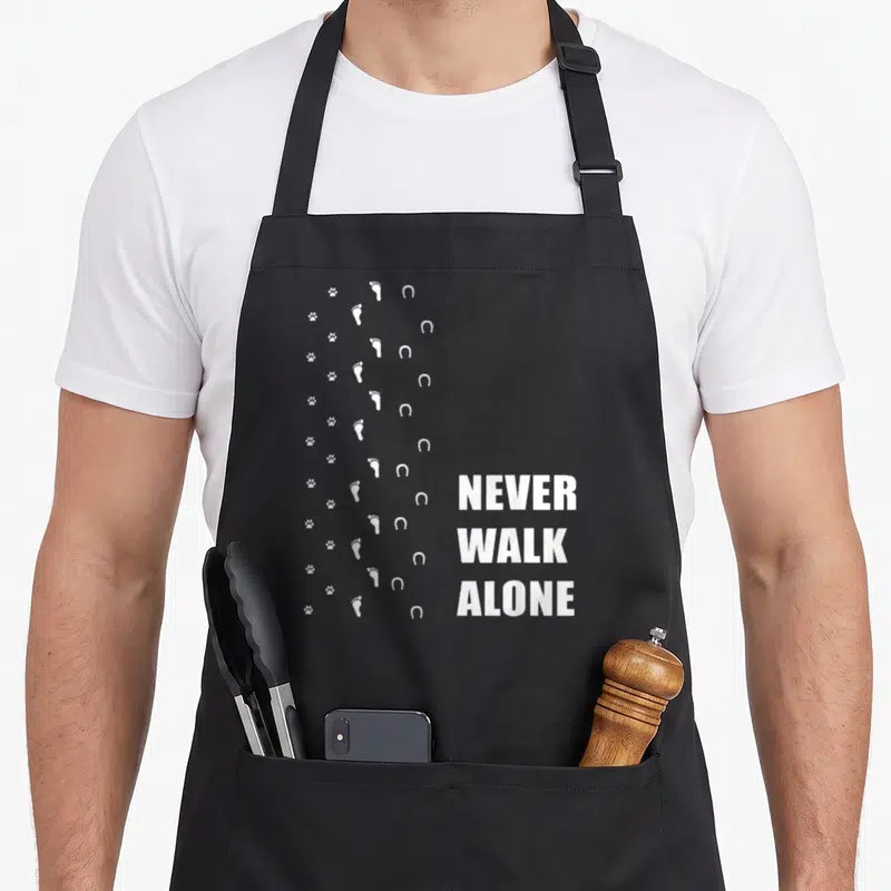 Tablier de cuisine noir avec traces blanches de pattes, pieds et fers à cheval et texte Never Walk Alone