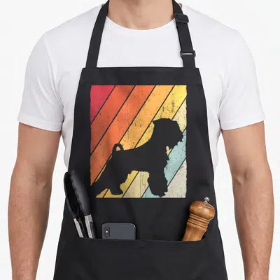 Tablier de cuisine noir avec silhouette grise de Schnauzer nain sur fond de bandes diagonales orange jaune et bleu pastel.