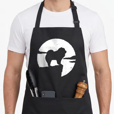 Tablier de cuisine noir avec silhouette de chien Chow Chow dans un cercle blanc texturé sur fond gris.