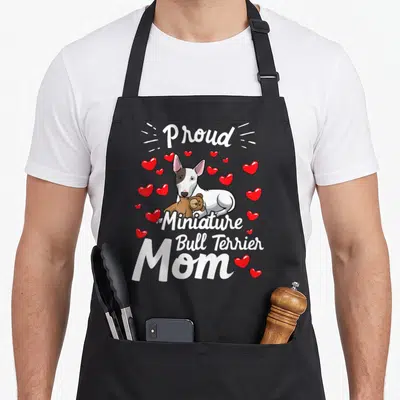 Tablier de cuisine noir avec illustration d'un Bull Terrier miniature tenant une peluche et des cœurs rouges autour.