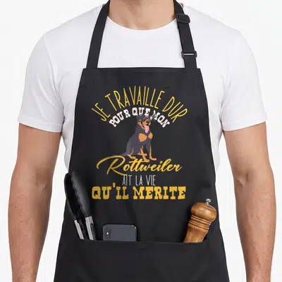 Tablier de cuisine noir avec illustration d'un Rottweiler souriant et texte jaune et blanc sur fond uni.