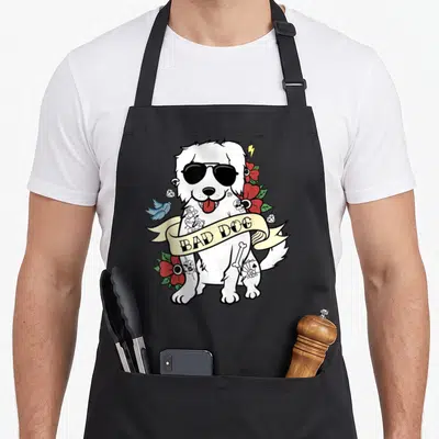 Tablier de cuisine noir avec illustration d'un chien blanc en style tattoo portant des lunettes noires et une banderole Bad Dog.