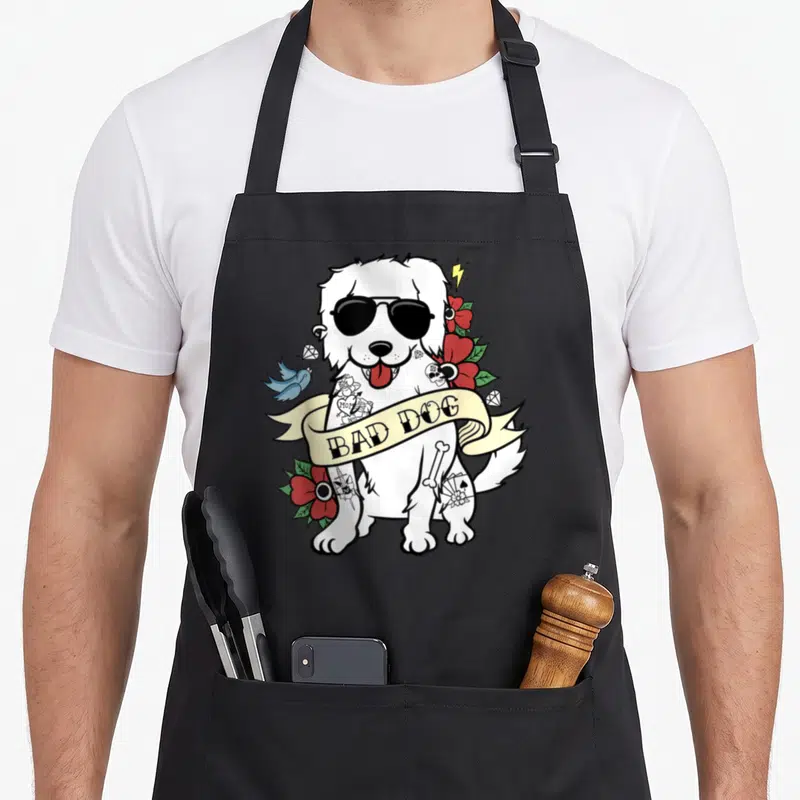 Tablier de cuisine noir avec illustration d'un chien blanc en style tattoo portant des lunettes noires et une banderole Bad Dog.