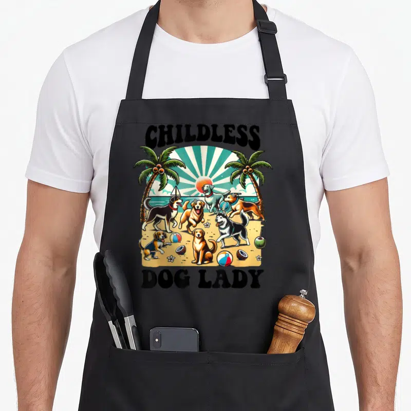 Tablier de cuisine noir avec illustration de chiens jouant sur une plage sous des palmiers et le texte Childless Dog Lady.