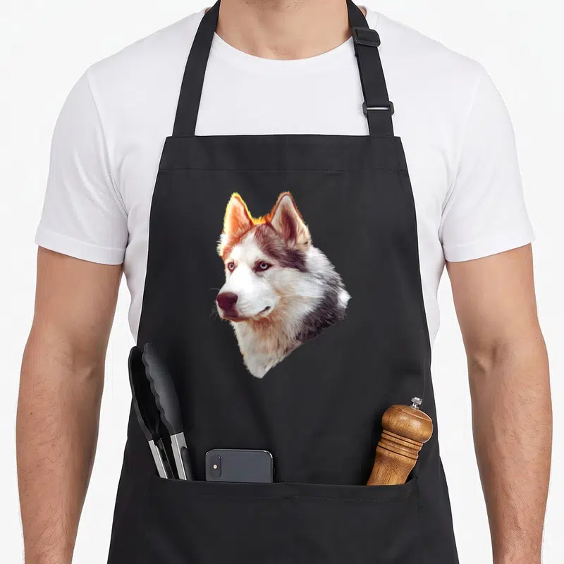 Tablier de cuisine noir avec l'illustration détaillée d'une tête de husky brun et blanc au regard intense.