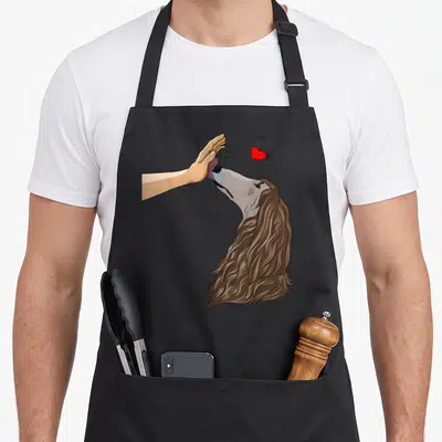 Tablier de cuisine noir avec illustration d'un lévrier afghan longiligne léchant une main humaine sous un petit cœur rouge.