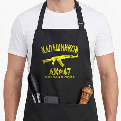 Tablier de cuisine noir avec illustration jaune d'un fusil d'assaut et texte en alphabet cyrillique.