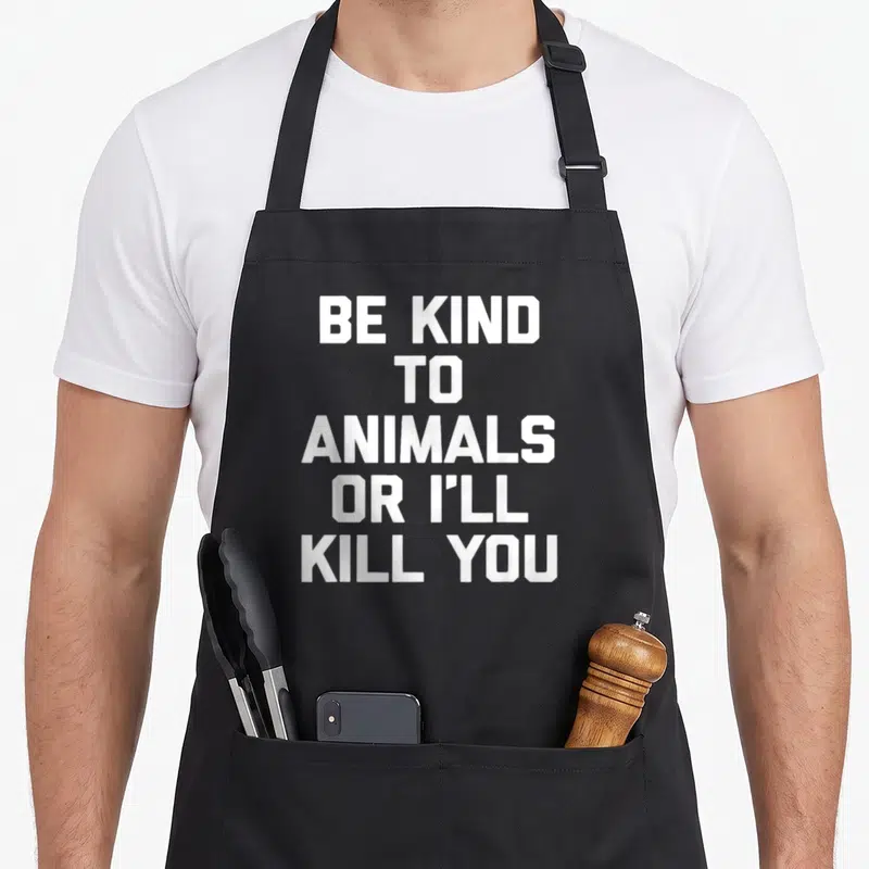 Tablier de cuisine noir avec inscription blanche Be Kind To Animals Or I'll Kill You en gros caractères capitales.