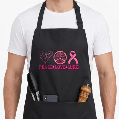 Tablier de cuisine noir avec un cœur texturé, un signe de paix et un ruban rose sur fond gris.