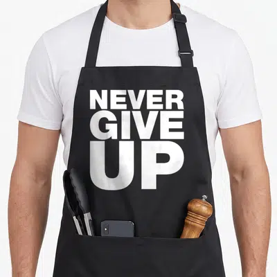 Tablier de cuisine noir avec l'inscription blanche Never Give Up en grandes lettres capitales stylisées.