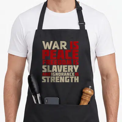 Tablier de cuisine noir avec texte rouge et beige « War is Peace Freedom is Slavery and Ignorance is Strength » imprimé au centre.