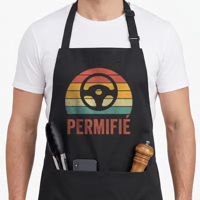 Tablier de cuisine noir avec illustration d'un volant devant un soleil couchant multicolore et le mot permifié en rouge.