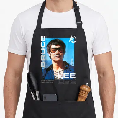 Tablier de cuisine noir avec portrait de Bruce Lee, lunettes et texte Moving be like water en typographie blanche.