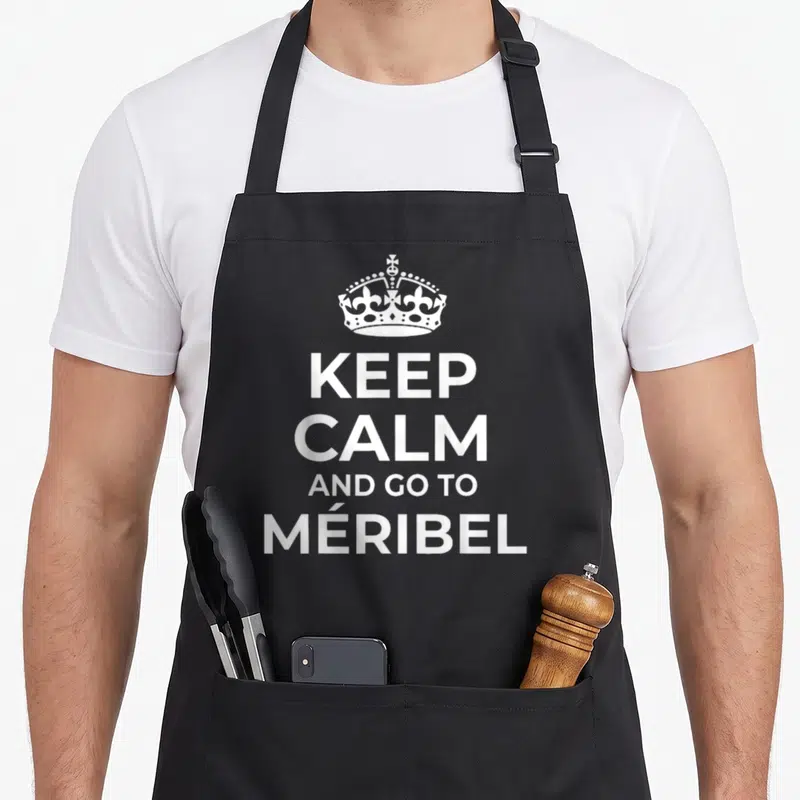 Tablier de cuisine noir avec inscription Keep Calm And Go To Meribel et une couronne blanche stylisée au centre.