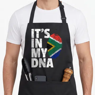 Tablier de cuisine noir avec une empreinte digitale formant le drapeau de l'Afrique du Sud et le texte It's in my DNA en blanc.