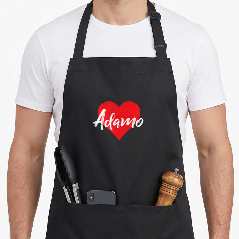 Tablier de cuisine noir avec un grand cœur rouge portant l'inscription blanche « I Love Adamo » en style manuscrit.