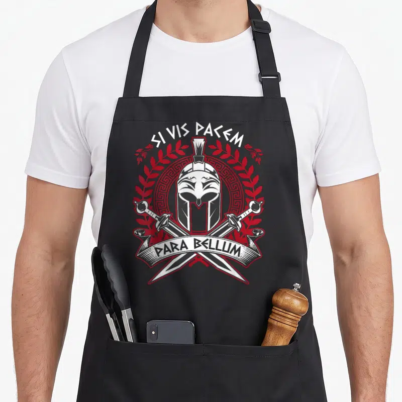 Tablier de cuisine noir orné d'un casque spartiate, de deux épées croisées et de la mention Si Vis Pacem Para Bellum en blanc et rouge.