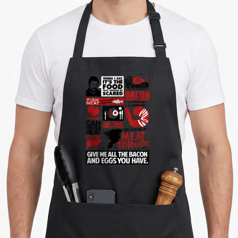 Tablier de cuisine noir avec illustrations rouges et noires de Ron Swanson, bacon, dinde et citations humoristiques en anglais.