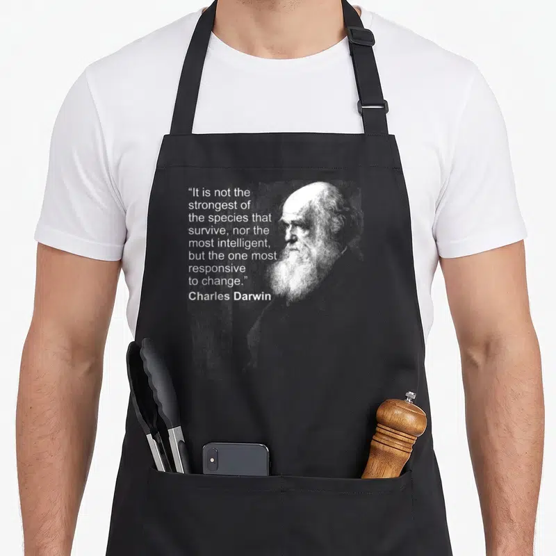 Tablier de cuisine noir avec portrait de Charles Darwin et sa citation sur l'évolution en typographie blanche.