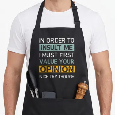 Tablier de cuisine noir avec inscription bilingue en blanc, bleu et orange sur fond uni.