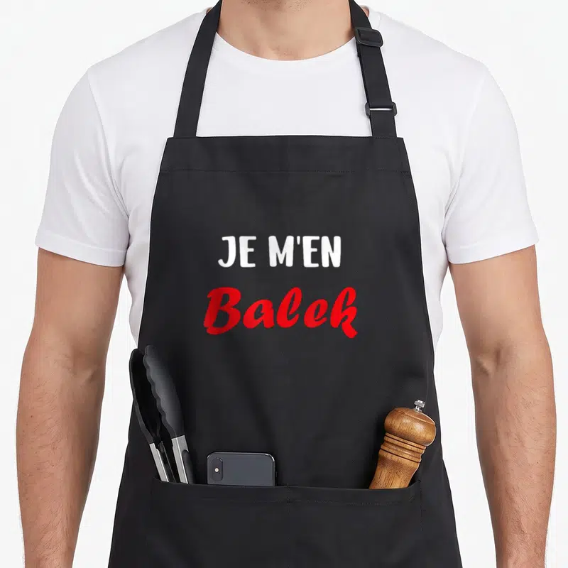 Tablier de cuisine noir avec le texte Je m'en Balek en blanc et rouge au centre.