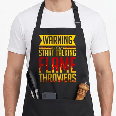 Tablier de cuisine noir avec une inscription graphique jaune et rouge évoquant des flammes et un message humoristique en anglais.