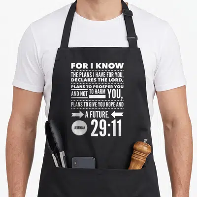 Tablier de cuisine noir avec le texte blanc For I Know The Plans I Have For You et la référence Jérémie 29:11 en bas à droite.