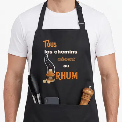 Tablier de cuisine noir avec une illustration de bouteille de rhum et le texte Tous les chemins mènent au rhum en orange et blanc.