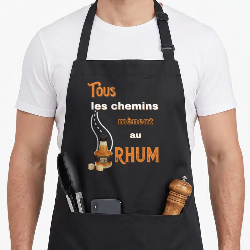 Tablier de cuisine noir avec une illustration de bouteille de rhum et le texte Tous les chemins mènent au rhum en orange et blanc.