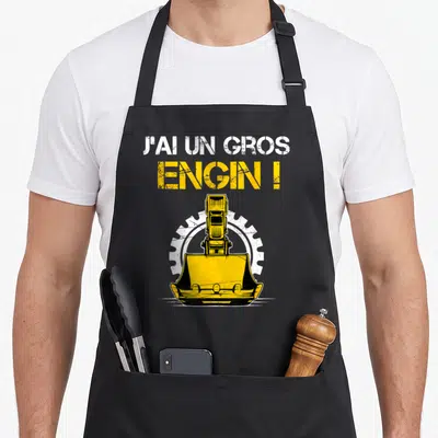 Tablier de cuisine noir avec illustration de tractopelle jaune et texte J'ai un gros engin. en typographie usée.