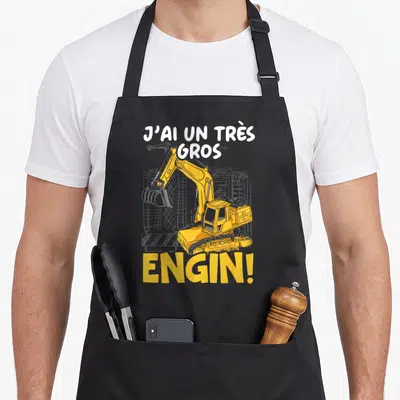 Tablier de cuisine noir avec une pelleteuse jaune et le texte J'ai un très gros engin imprimé en blanc et orange.