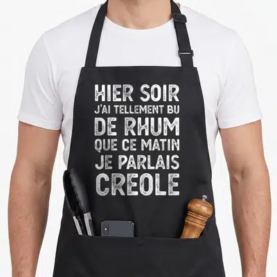 Tablier de cuisine noir avec texte blanc humoristique sur le rhum et la langue créole imprimé en gros caractères.