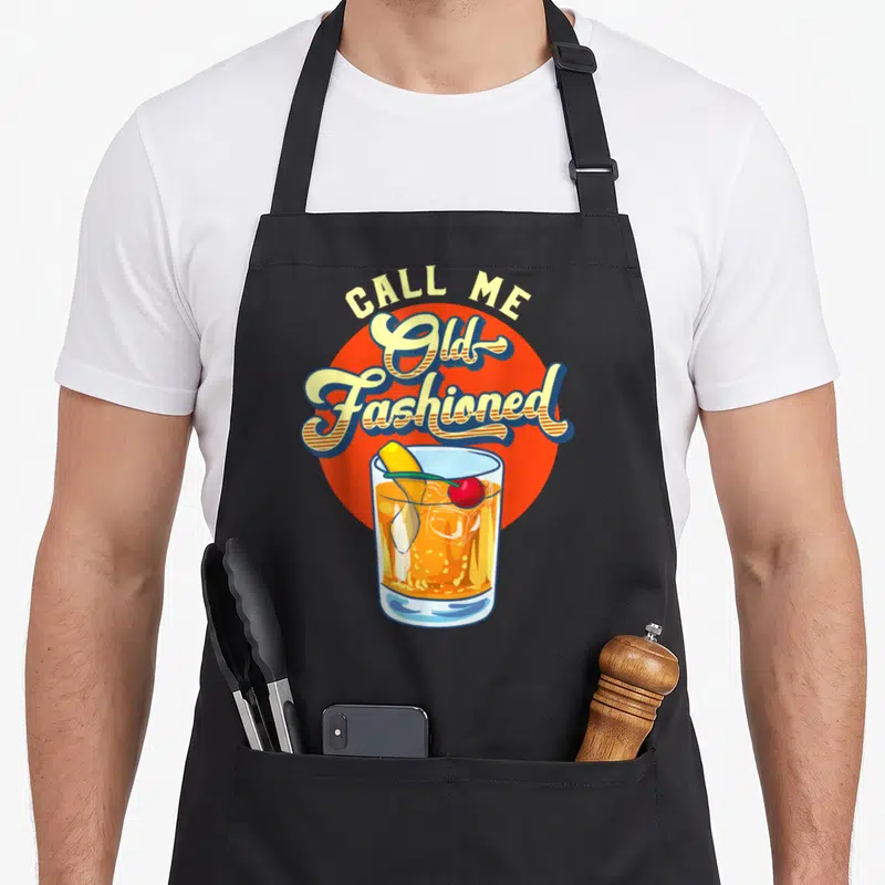 Tablier de cuisine noir avec illustration vintage d'un cocktail Old Fashioned et du texte Call Me Old Fashioned en lettres jaunes.