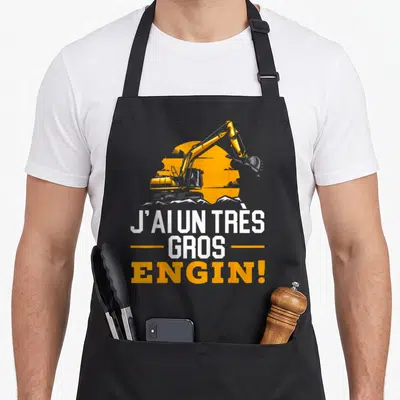 Tablier de cuisine noir avec illustration pelleteuse jaune et texte J'ai un très gros engin en blanc et orange.