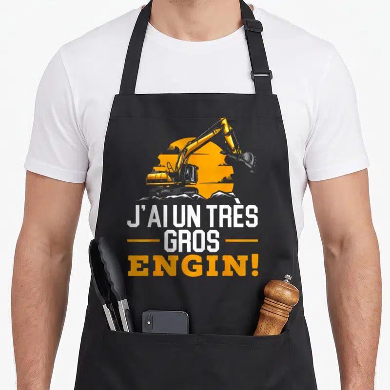 Tablier de cuisine noir avec illustration pelleteuse jaune et texte J'ai un très gros engin en blanc et orange.
