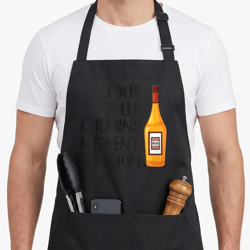 Tablier de cuisine noir avec une illustration de bouteille de rhum et le texte tous les chemins mènent au rhum imprimé en noir.
